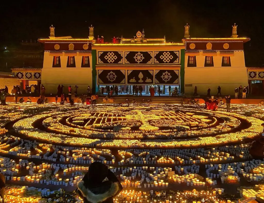 Monks and pilgrims lighting thousands of butter lamps at Jokhang Temple Square in Lhasa during the Tsongkhapa Butter Lamp Festival on a winter night in Tibet