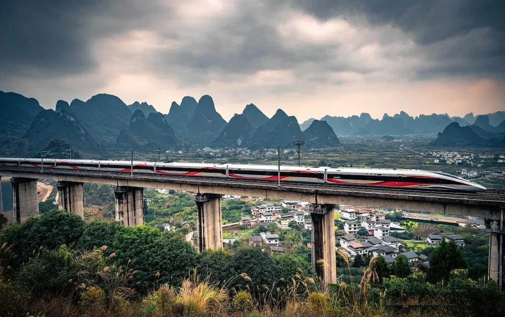 Motion shot of a sleek Fuxing Hao bullet train passing through the lush green karst mountain landscape of Yangshuo near Guilin, China.