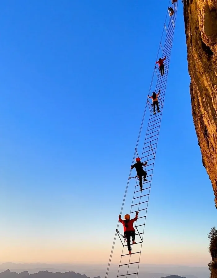 Via ferrata sky ladder experience in Zhangjiajie with travelers climbing a vertical steel ladder on a cliffside